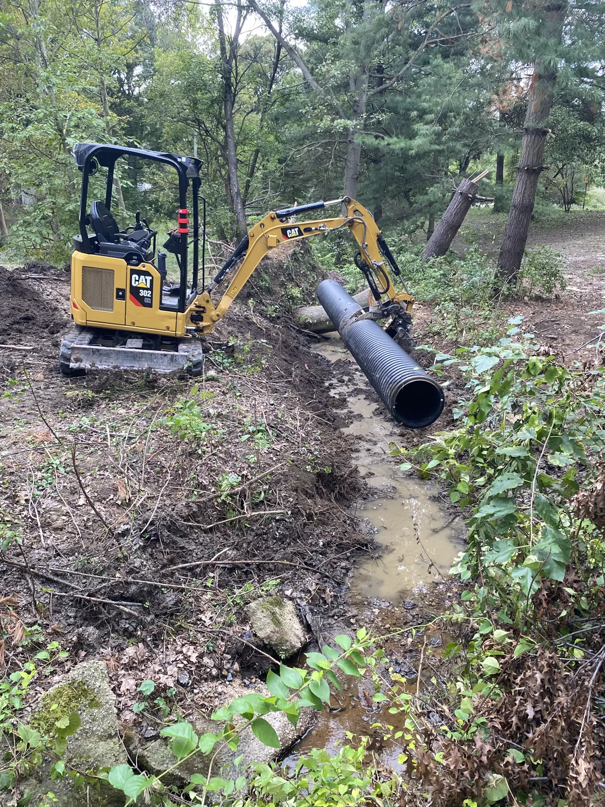 Mini excavator setting a corrugated culvert pipe in a ditch