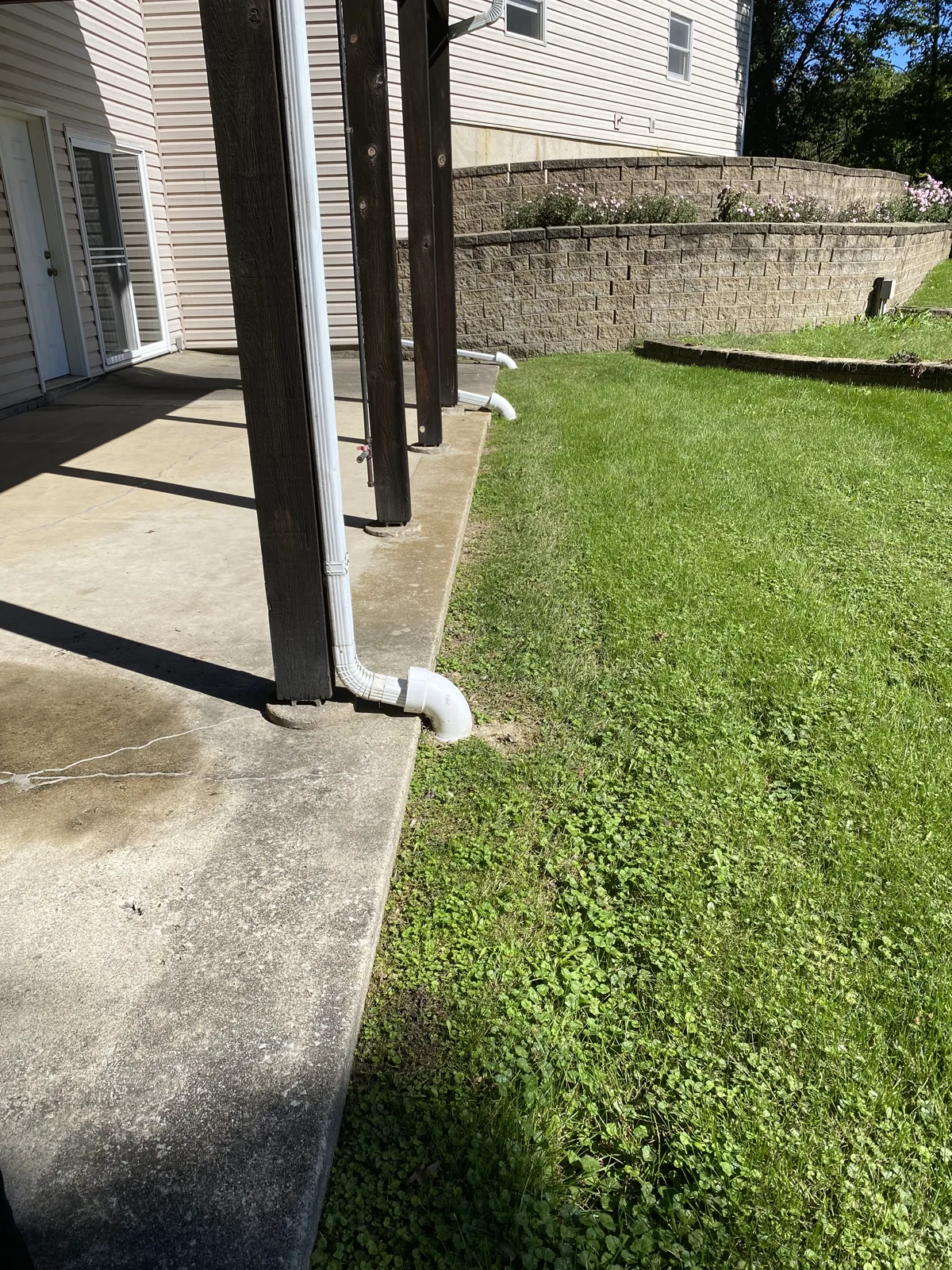 Downspout tied into a buried drain line at the edge of a patio