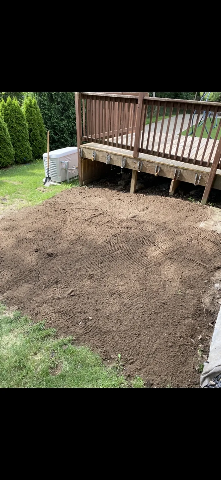 Graded dirt finished against the deck, with the generator and hedge beyond