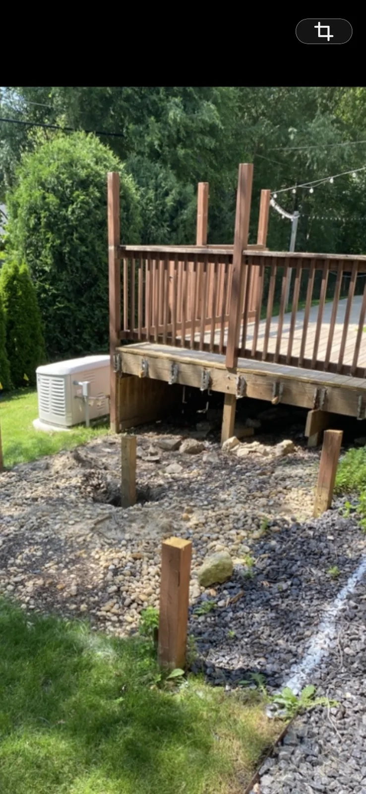 Post holes and gravel under a deck, with new posts set for the work