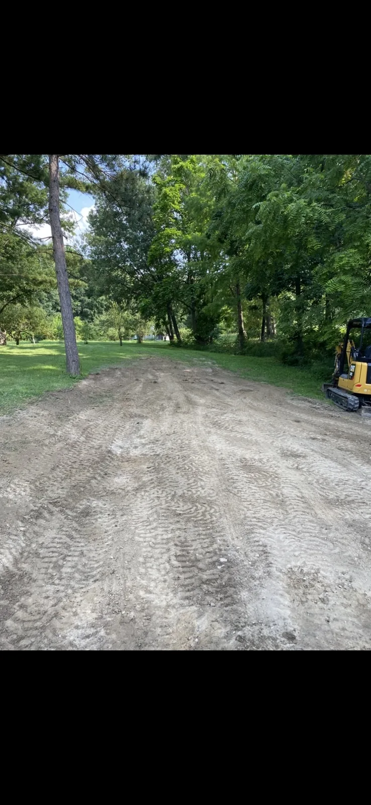Graded earth with machine tracks and a mini excavator at the edge of the trees
