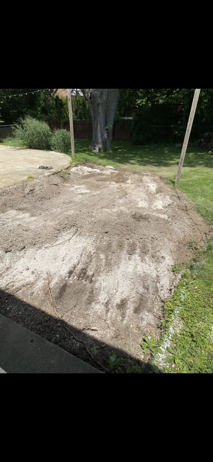 Leveled dirt and gravel cut in a backyard beside a patio and fence