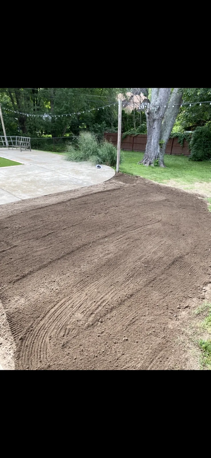 Finished grade in the backyard against the patio, tree, and fence
