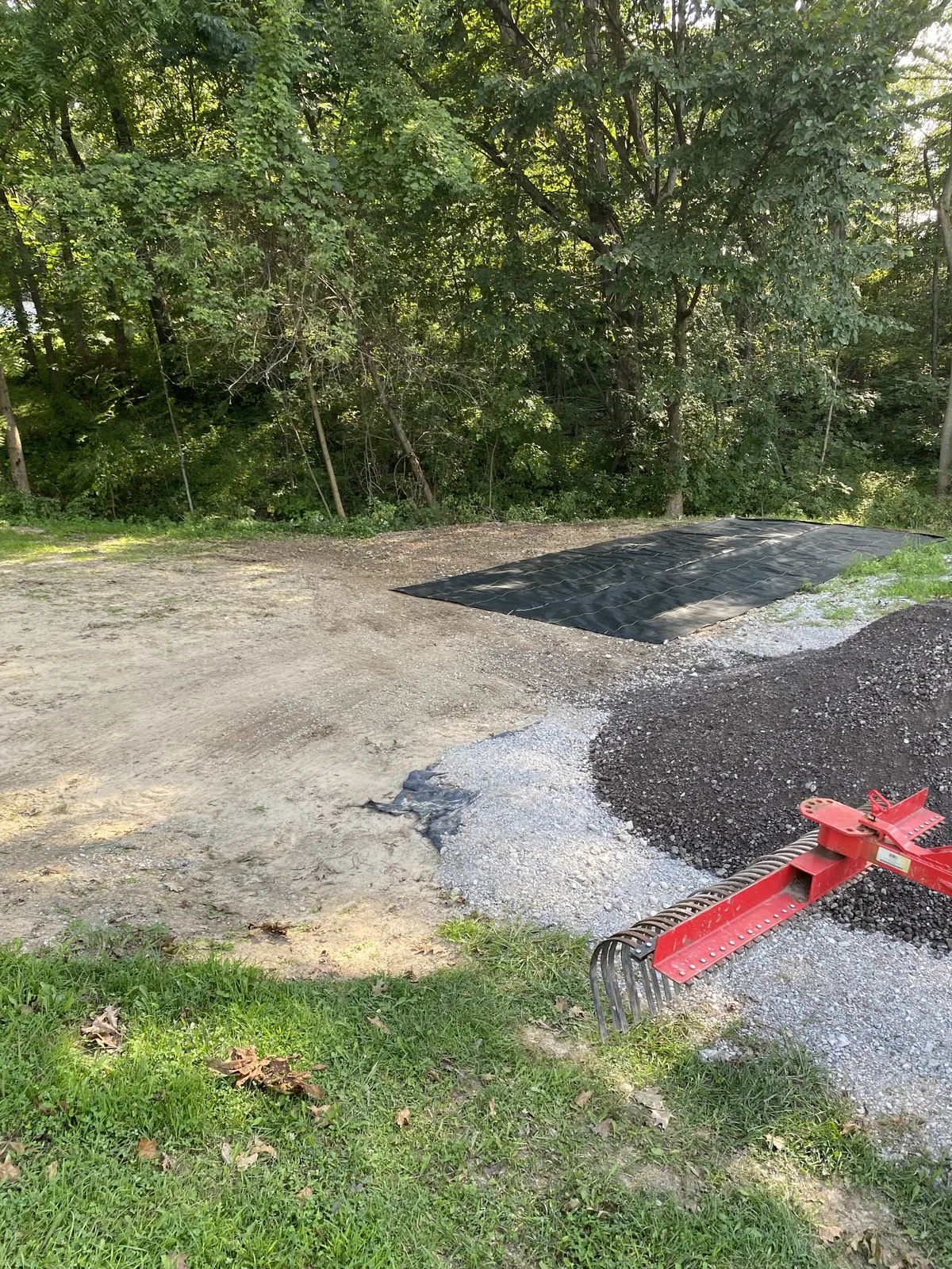 Parking pad under construction with fabric, stone, and millings at the tree line