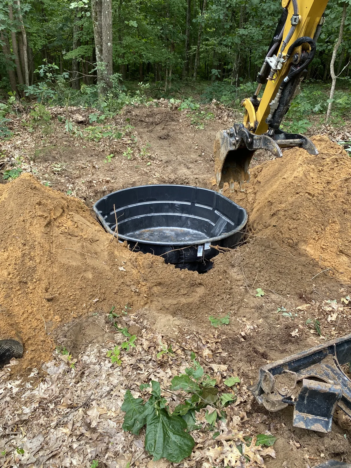 Excavator setting a 300-gallon wildlife water tank into a dug pit in the woods